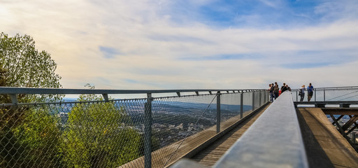 Fototapeta premium Panoramic view along the handrail of the wooden Rhine viewing platform at the peak of the hill next to the Ehrenbreitstein Fortress in Koblenz, Germany on a nice autumn day with a blue sky.