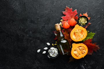 Pumpkin oil and pumpkins. Autumn vegetables. flat lay. On a black stone background. Top view. Free space for your text.