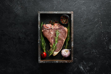 Raw T-bone steak on a black stone table. Top view. Free space for your text.