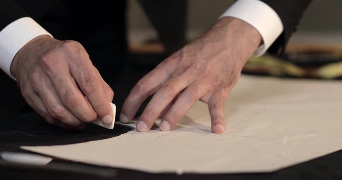 Footage of a tailor drawing lines on fabric and making some alterations arround the cut with his chalk