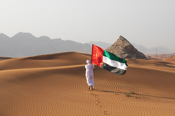Arab man holding the UAE flag in the desert celebrating UAE national day and Uae flag day. - obrazy, fototapety, plakaty