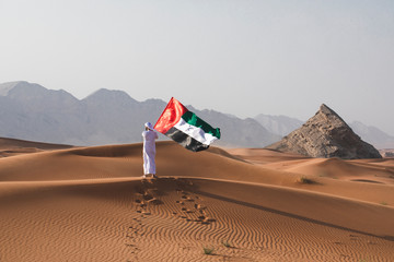 Arab man holding the UAE flag in the desert celebrating UAE national day and Uae flag day.