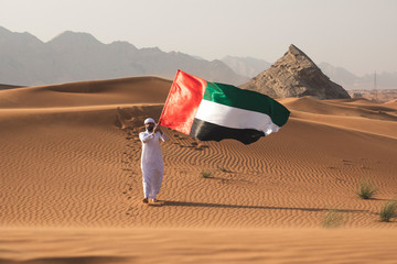 Arab man holding the UAE flag in the desert celebrating UAE national day and Uae flag day.