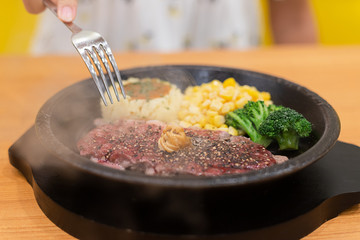 Meat steak with vegetable put on hot plate after cook make steam flow over, have fork ready to take piece of meat