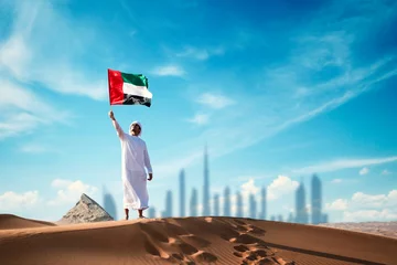 Foto op Plexiglas Arab man holding the UAE flag in the desert celebrating UAE national day and Uae flag day. © Moez