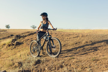 Obraz premium Girl on a mountain bike on offroad, beautiful portrait of a cyclist at sunset, Fitness girl rides a modern carbon fiber mountain bike in sportswear. Close-up portrait of a girl in a helmet and glasses