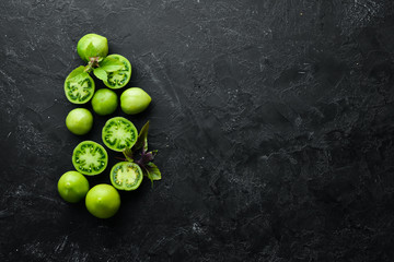 Fresh green tomatoes on black stone background. Green vegetables. Top view. Free space for your text.
