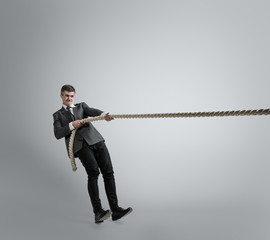 Time for strenght. Man in office clothes training with ropes on grey background. Get target, overcoming problems, deadlines. Businessman in motion, action. Sport, healthy lifestyle, working.