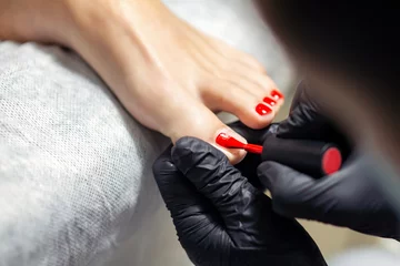 Keuken foto achterwand Pedicure Handen in zwarte handschoenen doen rode pedicure of manicure op de tenen van de vrouw, close-up.