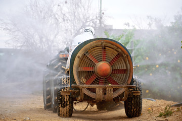Rear view of farmer in a tractor spraying pesticide on lemon plantation in Spain. Weed insecticide...