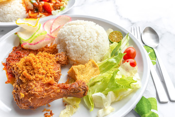 Ayam Penyet is Indonesian, East Javanese cuisine - consisting of fried chicken that is smashed with the pestle against mortar to make it softer, served with sambal chilli. Food on table concept.