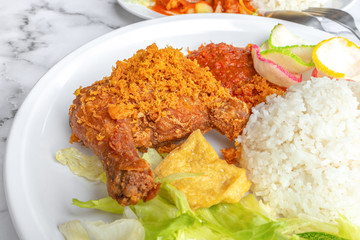 Ayam Penyet is Indonesian, East Javanese cuisine - consisting of fried chicken that is smashed with the pestle against mortar to make it softer, served with sambal chilli. Food on table concept.