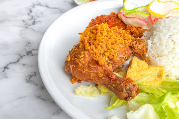Ayam Penyet is Indonesian, East Javanese cuisine - consisting of fried chicken that is smashed with the pestle against mortar to make it softer, served with sambal chilli. Food on table concept.