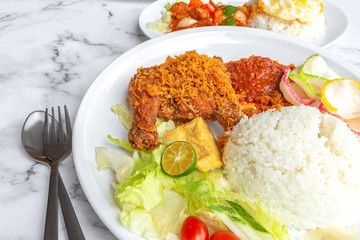 Ayam Penyet is Indonesian, East Javanese cuisine - consisting of fried chicken that is smashed with the pestle against mortar to make it softer, served with sambal chilli. Food on table concept.