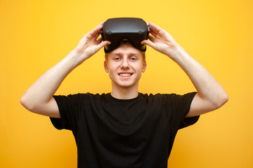 guy in VR glasses on a yellow background holds a device and smiles, a gamer starts a game and puts on virtual reality glasses