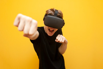 joyful young guy in VR glasses on a yellow background plays in virtual boxing, a gamer uses modern...