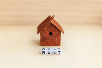 Miniature toy model house with inscription RENT letters word on wooden backdrop. Eco Village, abstract environmental background. Real estate mortgage property insurance sweet home ecology rent concept