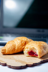 croissants bitten with strawberry jam with dry wheat on a wooden board on a laptop background