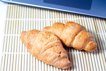 croissants bitten with strawberry jam with dry wheat on a bamboo mat on a laptop background