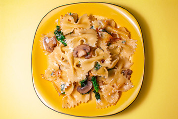 butterfly pasta with fried mushrooms, green spinach on a yellow plate on an orange background