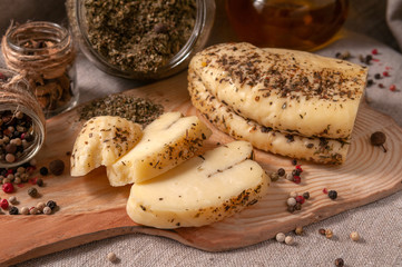 Halumi cheese with spices is sliced ​​on a wooden board. Decorated with spices. In the background glass jars with spices and olive oil. Close-up.