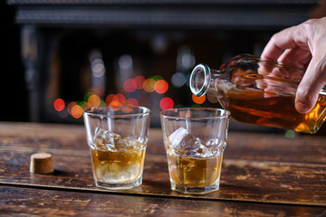 The waiter pours whiskey in a bar on a wooden table in an old-fashioned glass
