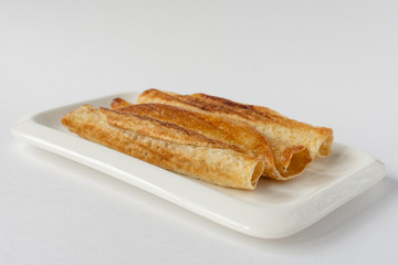 Fried pancakes roll into a tube on a white plate with a white background.