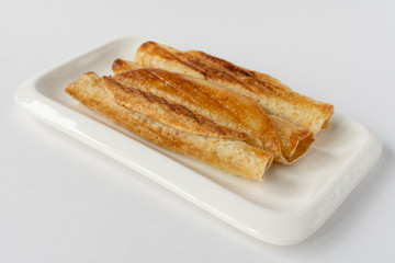 Fried pancakes roll into a tube on a white plate with a white background.