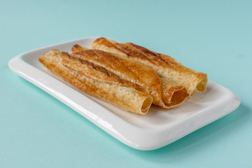 Fried pancakes roll into a tube on a white plate with a blue background.