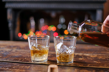 The waiter pours whiskey in a bar on a wooden table in an old-fashioned glass