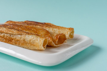 Fried pancakes roll into a tube on a white plate with a blue background.