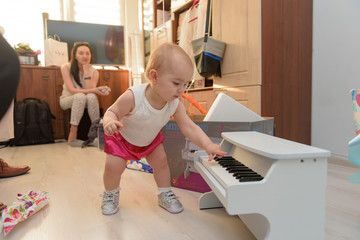 beautiful baby girl playing toy piano in light room. Authentic image