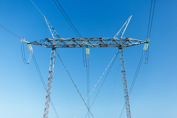 Close-up of a high voltage power line pole isolated against clear blue sky. No visible horizon