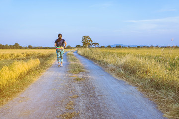 Obraz premium Back view of woman running and exercising on the path through the rice fields in the evening.