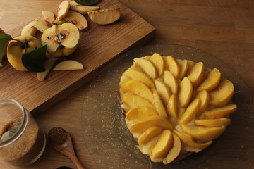 Quince tarte tatin served with whipped cream, quince fruits and walnuts on a wooden surface. Rustic style.