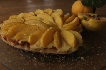 Quince tarte tatin served with whipped cream, quince fruits and walnuts on a wooden surface. Rustic style.