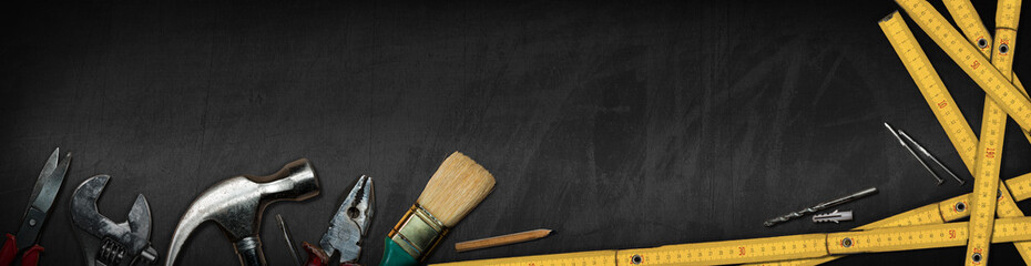 Group of hand tools on a black blackboard with copy space and dark shadows. Home improvement and do...