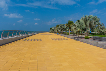 Marjan Island in Ras al Khaimah, United Arab Emirates boardwalk along the Arabian Gulf (Persian Gulf) on a blue sky day with green palm trees and plants.