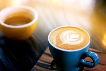 cup of cappuccino with latte art on wooden background. Beautiful foam, greenery ceramic cups, stylish toning, place for text.
