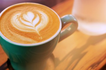 cup of cappuccino with latte art on wooden background. Beautiful foam, greenery ceramic cups, stylish toning, place for text.