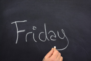 Woman's hand writing the day of the week on a blackboard with white chalk, friday
