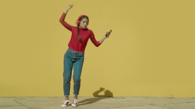 Young Happy Latin Woman wearing red shirt and jeans and red converse shoes starts dancing with a yellow background wall on a sunny day wide-angle shot