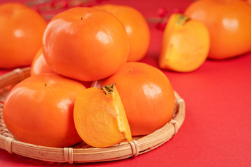 Fresh beautiful sliced sweet persimmon kaki isolated on red table background and bamboo sieve, Chinese lunar new year design concept, close up.