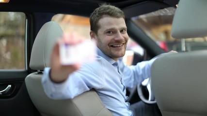 young happy man sitting in the car and showing his new driver license with thumb up sign