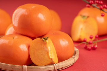 Fresh beautiful sliced sweet persimmon kaki isolated on red table background and bamboo sieve, Chinese lunar new year design concept, close up.