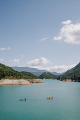 Fototapeta na wymiar People practicing sport (kayak) on a sunny day in a blue water lake surrounded by mountains on summer
