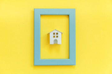 Simply design with miniature white toy house in blue frame isolated on colorful trendy yellow background. Mortgage property insurance dream home concept. Flat lay top view copy space