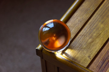 A crystal globe resting on a wooden chest reflecting an orange light 