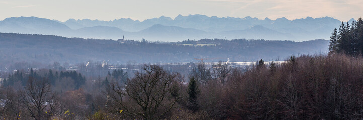 GUT RIEDEN, BAVARIA / GERMANY - December 11, 2019: Panorama of autumn landscape of the alpine foreland close to Lake Starnberg. In the foreground trees, in the far distance the misty bavarian alps.