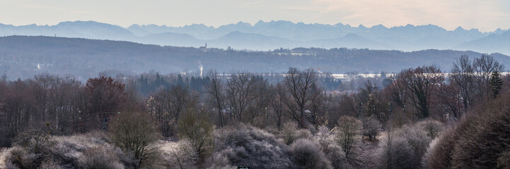 Fototapeta na wymiar GUT RIEDEN, BAVARIA / GERMANY - December 11, 2019: Panorama of alpine foreland of upper bavaria. Winter landscape with trees in the foreground and the alps in the far distance. Misty and foggy.